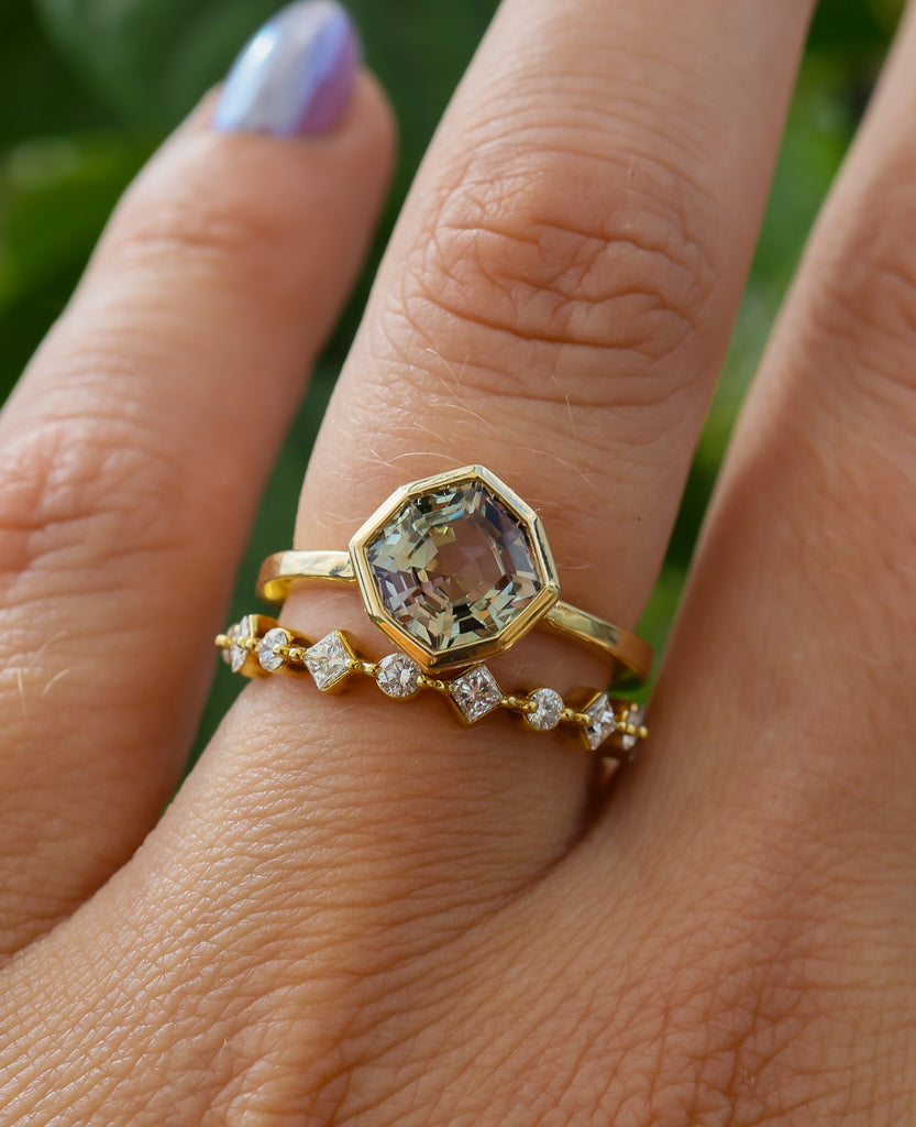 Gold ring with a large gemstone on a finger against a blurred green background