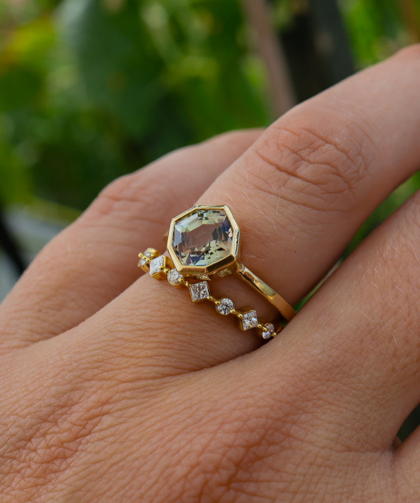Gold ring with a large gemstone on a person's finger against a blurred green background